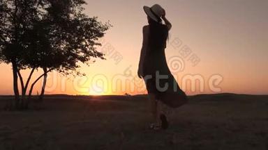 一位戴着帽子和长裙的年轻女子在田野上朝夕阳走来的剪影